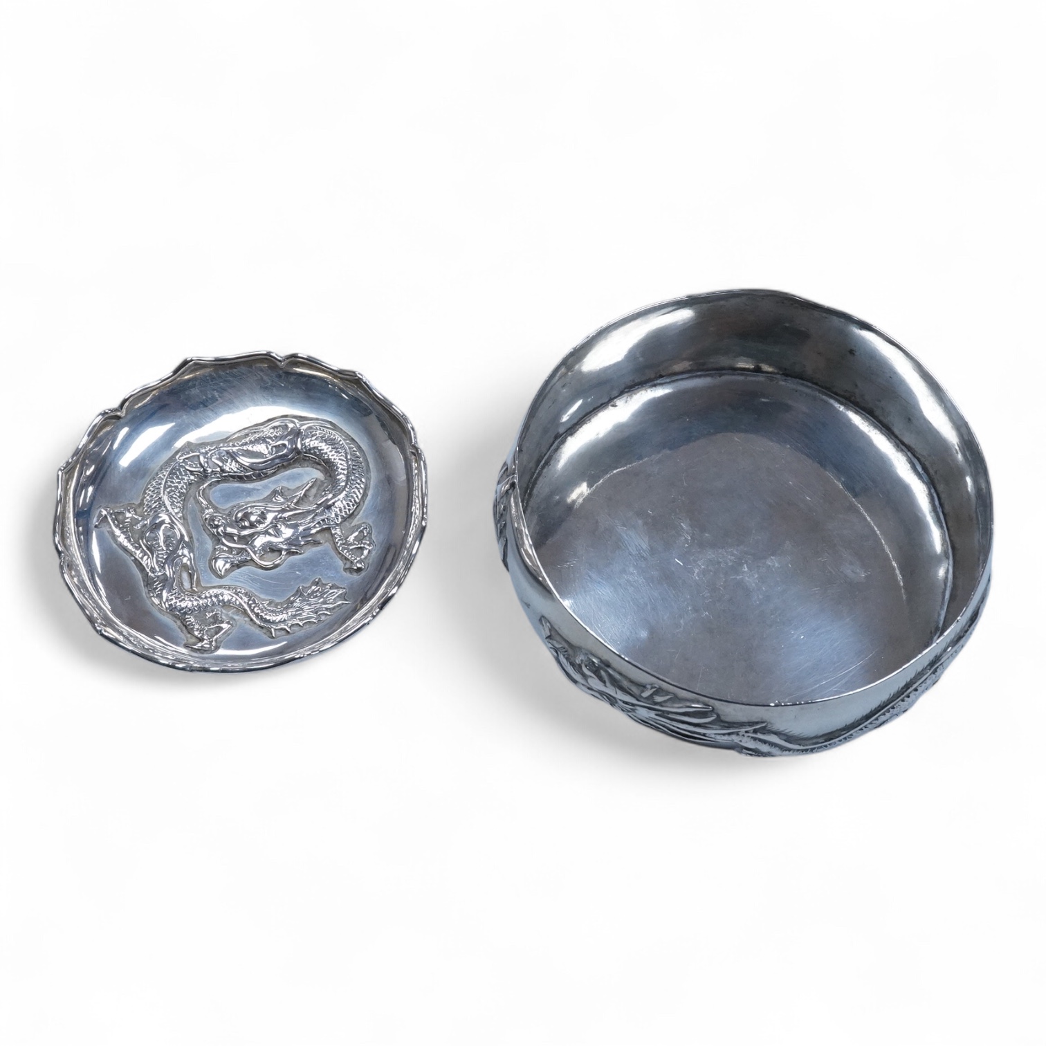 An early 20th century Chinese Export white metal small trinket dish with dragon decoration, by Sing Fat, diameter 66mm, together with a larger Chinese Export white metal trinket dish, maker Tien Shing?.